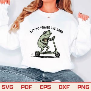 May include: White sweatshirt with the text "OFF TO PRAISE THE LORD" above a cartoon frog riding a scooter while holding a book. The frog is green and the scooter is gray.