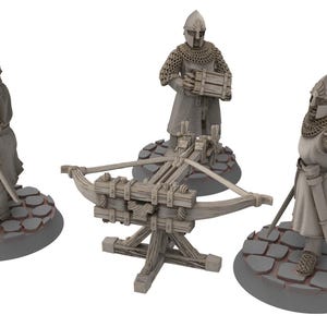 Może przedstawiać: Trzy miniaturowe figurki średniowiecznych żołnierzy, dwóch z mieczami i jeden z kuszą, stojących na okrągłych podstawach o kamiennej fakturze. Kusza jest wykonana z drewna i ma przymocowaną strunę.