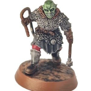 May include: A miniature orc figurine with green skin and a grimace. It wears chainmail and holds a whip and a mace. The figure is mounted on a brown base, depicting a fantasy character. The figure is likely used in tabletop games.