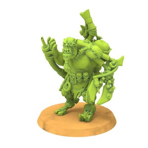 Puede incluir: Figura en miniatura verde de una criatura de fantasía, posiblemente un orco. La figura está posada sobre una base circular marrón, con elementos mecánicos y tecnológicos integrados en su diseño. Tiene un arma y lleva gafas.