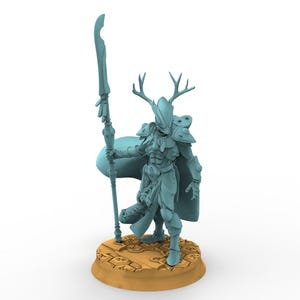 Könnte beinhalten: Eine hellblaue Miniaturfigur eines Kriegers mit einem Helm mit großem Geweih, der einen langen Speer in der Hand hält. Die Figur trägt eine detaillierte Rüstung und einen wehenden Umhang und steht auf einem runden, strukturierten beigen Sockel.