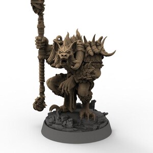 May include: A detailed brown fantasy figurine of a creature with bat-like ears, horns, and a staff. The figurine is crouched on a rocky base, with intricate details on its fur and armor. The staff is tall and detailed.