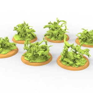 May include: Six miniature green dinosaur figurines on tan circular bases. The dinosaurs are in various poses, some standing and others lying down. The figurines are likely for tabletop gaming or model building.