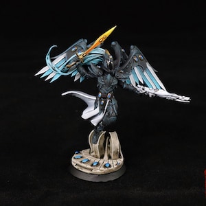 May include: A painted miniature figurine of a winged warrior in dark armor, holding a bright yellow sword aloft and a white rifle. The figure features flowing light blue hair, a white cape, and stands on a stone-colored base with blue accents.