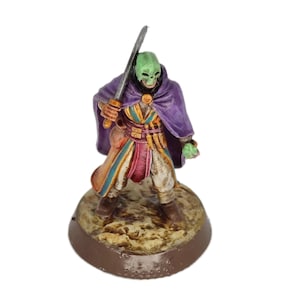 May include: A painted miniature figure of a person wearing a purple cloak and holding a sword. The figure has a green mask and is standing on a brown base.