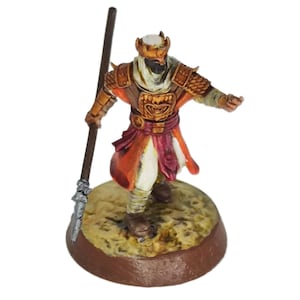May include: A painted miniature figurine of a warrior wearing a golden helmet, a white robe, and a red sash. The warrior holds a spear in his right hand and stands on a brown base.