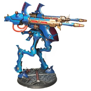 May include: A painted miniature sci-fi walker robot featuring a vibrant blue and metallic gold color scheme. The model has two long cannons mounted on top, orange tubing details, and stands on a circular base with a textured hexagonal pattern.