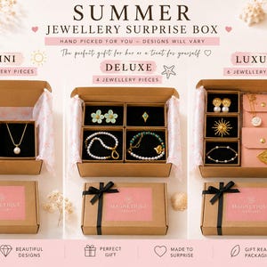 May include: Three cardboard gift boxes labeled Mini, Deluxe, and Luxury, each containing assorted gold-toned jewelry pieces like necklaces, bracelets, and earrings. The boxes feature pink labels with the text Magnetique Jewellery and black ribbons.