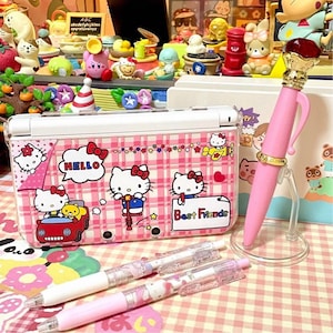 May include: A pink Hello Kitty themed pen with a gold-colored top and a red gem. A pink and white Nintendo DS case with Hello Kitty graphics and the words "Best Friends" is also visible, along with two pens.