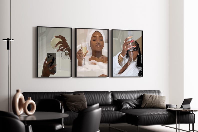May include: Three framed art prints depicting women enjoying champagne. One print shows a woman in a bathtub, another shows a woman taking a selfie with a glass, and the third shows a woman drinking champagne. The prints are displayed above a black leather sofa.