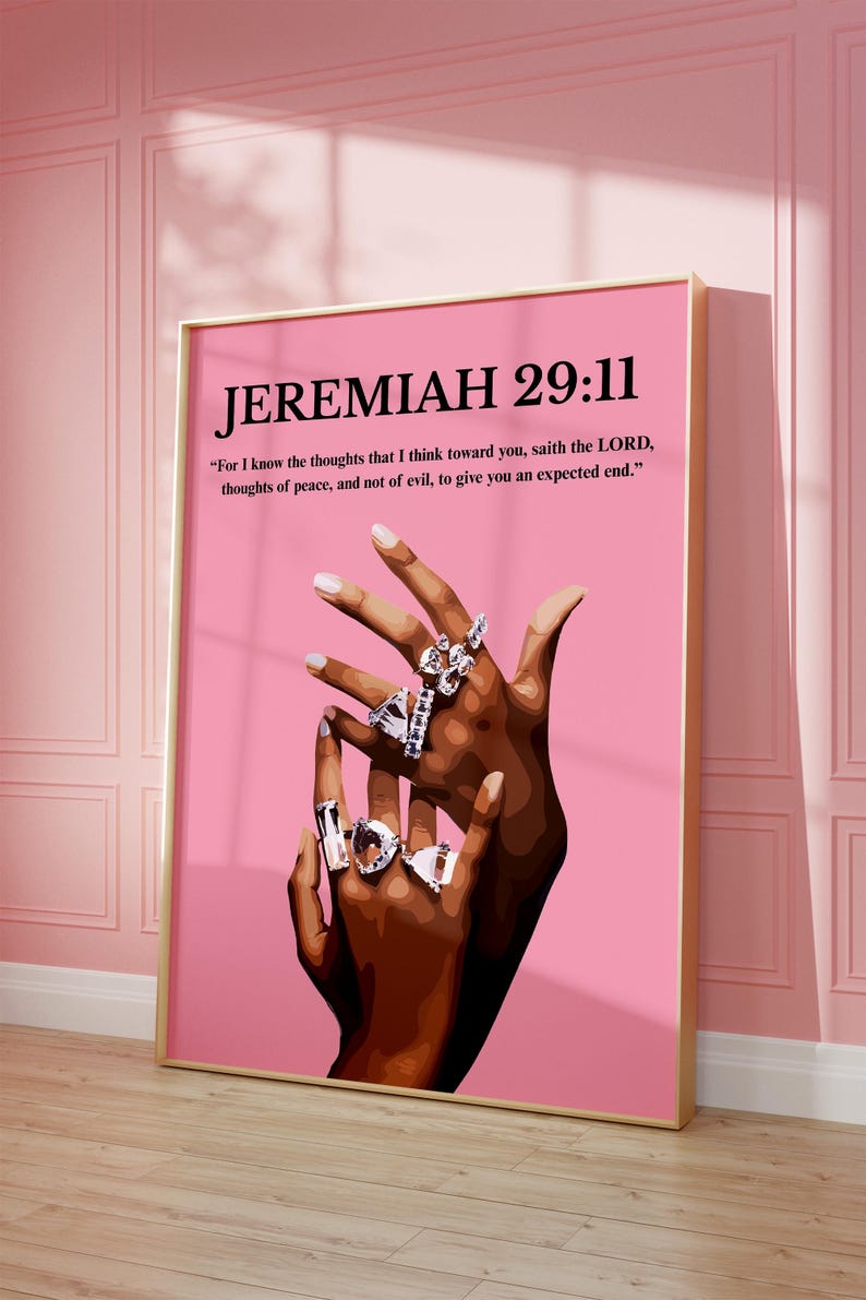 May include: A framed print with the text "JEREMIAH 29:11" and a quote on a pink background. The artwork features a pair of hands adorned with multiple silver rings. The frame is gold.