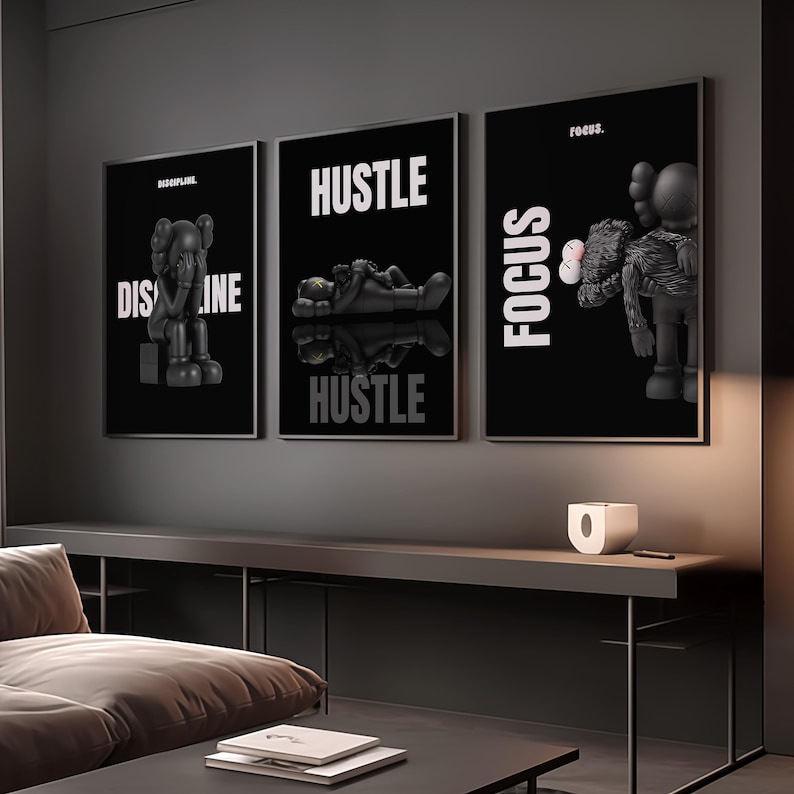 May include: Three framed black and white art prints with the words "DISCIPLINE", "HUSTLE", and "FOCUS". Each print features a stylized figure. The prints are displayed above a dark gray console table.