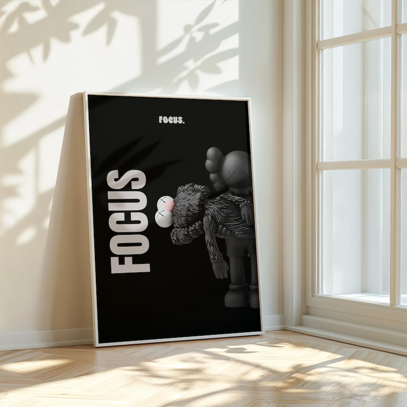 May include: Black framed art print featuring a black background with the word "FOCUS" in white vertical text. The print includes a grayscale illustration of a cartoon figure holding another figure. The word "focus." is written at the top.