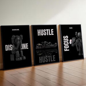 May include: Three framed black and white art prints. Each print features a black figure with white text. The prints read "DISCIPLINE", "HUSTLE", and "FOCUS". The figures are in different poses.