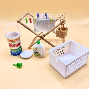 May include: A miniature laundry set with a wooden clothes drying rack, a white laundry basket, a white bucket with a green lid, a green funnel, a bottle of laundry detergent labeled "Soft", and a basket with a wicker texture.
