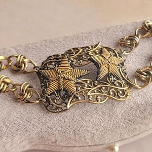 May include: A gold-coloured vintage bracelet with a central filigree design and two star motifs. The bracelet has a chain link design and a small bird charm. The clasp is a hook and eye closure.