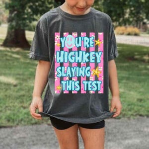 A young person wearing a gray t-shirt with a colorful graphic design and text printed on it.