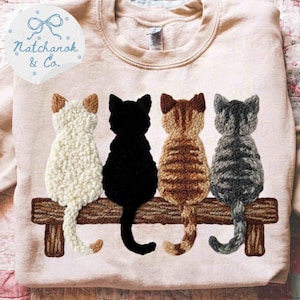 Könnte beinhalten: Hellrosa Sweatshirt mit einer Stickerei von vier Katzen, die auf einer Holzbank sitzen. Die Katzen sind weiß, schwarz, braun getigert und grau getigert. Der Text "Natchanok & Co." befindet sich in einem blauen Kreis oben links.