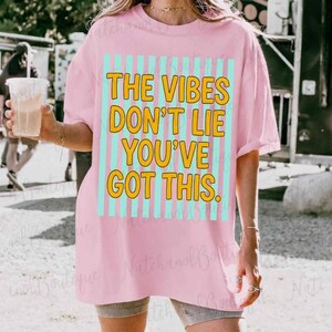 A person wearing a pink t-shirt with a motivational quote printed on it, holding a drink.