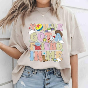 A woman wearing a t-shirt with a colorful graphic design that says "You'll Got a Friend in Me".