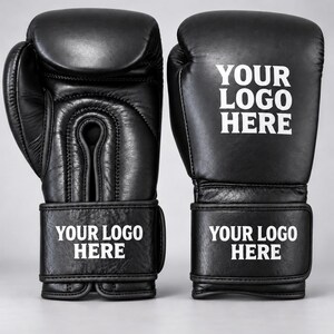 May include: A pair of black boxing gloves featuring white text that reads YOUR LOGO HERE on the wrist strap and the back of the hand. The gloves have a smooth finish with visible stitching details and a secure wrap-around closure system.