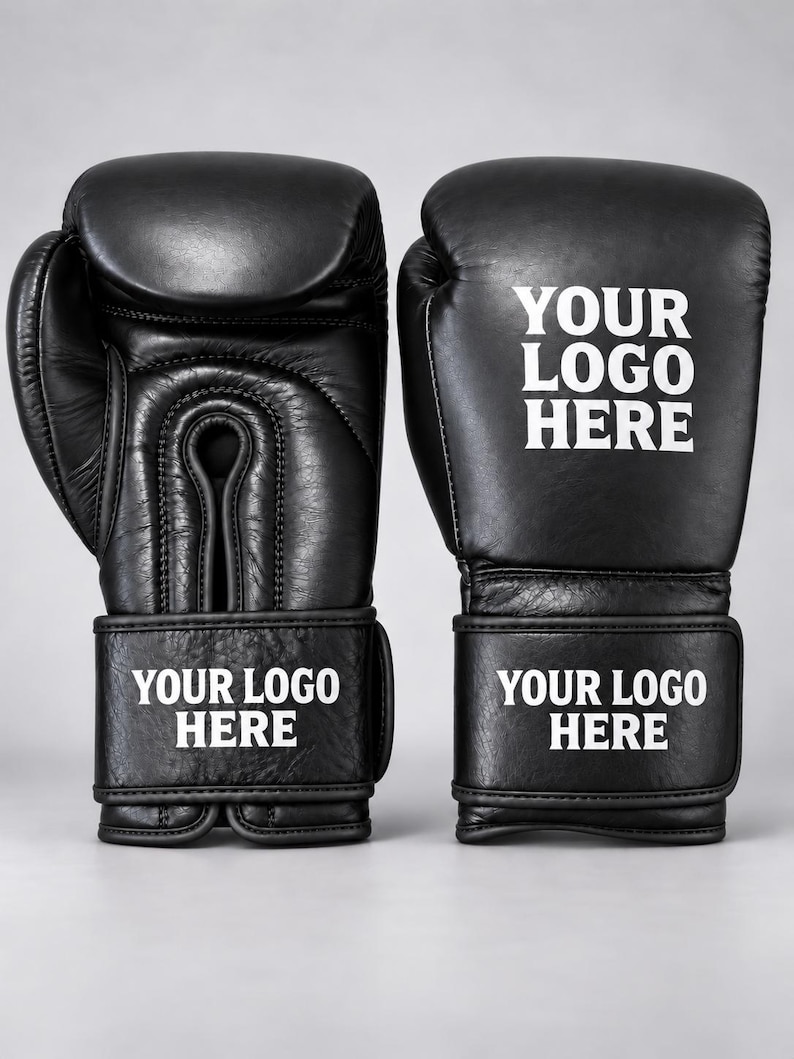 May include: A pair of black boxing gloves featuring white text that reads YOUR LOGO HERE on the wrist strap and the back of the hand. The gloves have a smooth finish with visible stitching details and a secure wrap-around closure system.
