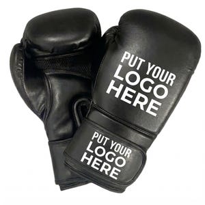 Puede incluir: Un par de guantes de boxeo negros con el texto blanco "PUT YOUR LOGO HERE". Los guantes son de cuero y tienen un diseño acolchado. Los guantes están diseñados para boxeo y otros deportes de combate.