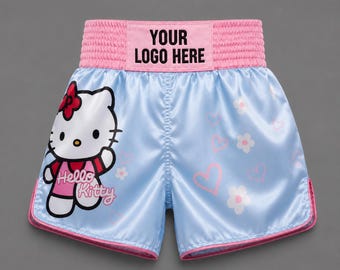 May include: Light blue satin athletic shorts with a pink elastic waistband featuring the text YOUR LOGO HERE. The left leg displays a Hello Kitty graphic, while the right leg features white flower and pink heart patterns with pink trim.