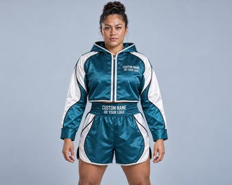 May include: A teal and white satin cropped zip-up hoodie and matching athletic shorts set. The hoodie features a front zipper and white panels, with the text CUSTOM NAME OR YOUR LOGO printed on the chest and the waistband of the shorts.