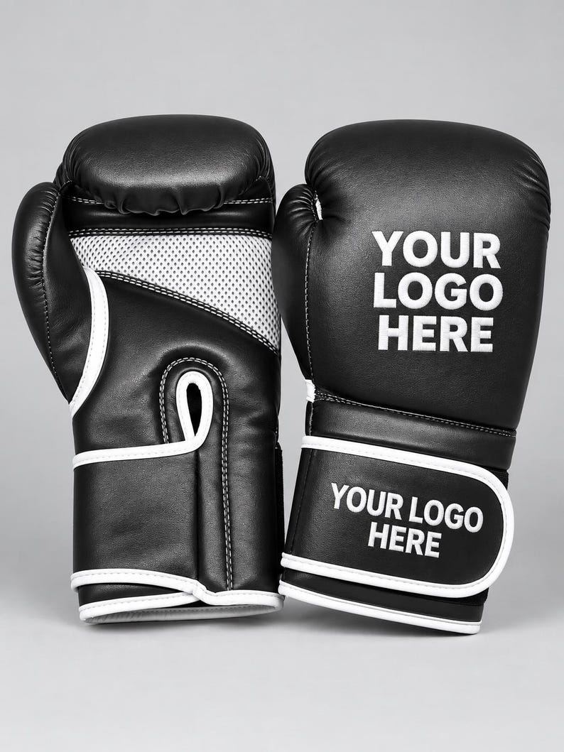 May include: A pair of black boxing gloves with white trim and mesh palm detailing. The gloves feature the white text "YOUR LOGO HERE" printed on the back of the hand and on the adjustable wrist strap, providing a clear area for custom branding.
