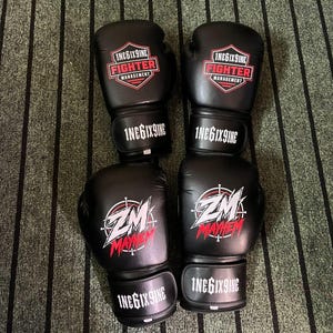 May include: Two pairs of black boxing gloves. The top pair features a red and white shield logo with the text 1NEGIX9INE FIGHTER MANAGEMENT. The bottom pair displays a white and red ZM MAYHEM graphic. All wrist straps are printed with 1NEGIX9INE.