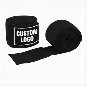 Puede incluir: Dos vendas negras para las manos, una enrollada y la otra parcialmente desenrollada. La venda enrollada tiene una etiqueta en blanco y negro con el texto "CUSTOM LOGO". Las vendas están hechas de tela acanalada.