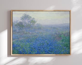 May include: A framed landscape painting depicting a vast field of bluebonnet flowers under a soft, hazy sky. The scene features clusters of green trees in the distance and rolling hills, rendered in muted tones of blue, green, and pale yellow.