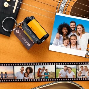 Pode incluir: Um porta-chaves com um design de rolo de filme, o texto "Portra 200 EXP" e um código Spotify. O porta-chaves está preso a uma guitarra. Uma foto de família está ao lado do porta-chaves. Uma tira de filme com fotos de família está na parte inferior.