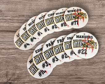 May include: A collection of 14 white round ornaments with the words "Maryland Intensity" and a number on each. The ornaments feature a red and black Maryland state flag design and a red claw mark.