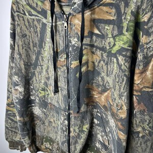 Puede incluir: Sudadera con capucha y cremallera con estampado de camuflaje. La chaqueta tiene una capucha con cordones, una cremallera frontal completa y dos bolsillos delanteros. El dise&ntilde;o de camuflaje incorpora tonos de verde, marr&oacute;n y gris.