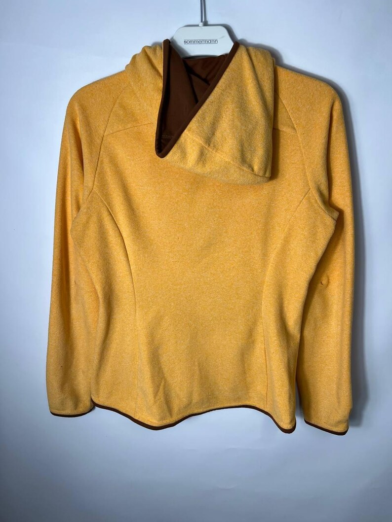May include: Mustard yellow hooded sweatshirt with a brown interior lining and trim. The long-sleeved top is hanging on a white hanger against a light gray background. The sweatshirt has a textured appearance.