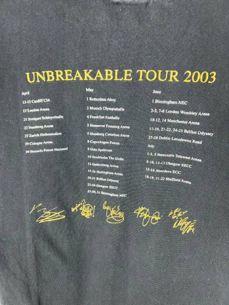 May include: A black t-shirt featuring yellow text that reads UNBREAKABLE TOUR 2003. Below the title, a list of concert dates and locations for April, May, June, and July is printed in white. Six yellow signatures are displayed at the bottom.