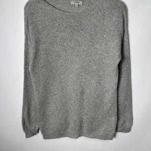 May include: A long-sleeved gray sweater with a wide boat neckline and a ribbed hem. The garment features a soft, heathered knit texture and includes a small interior brand label at the neck that reads Bartolini with the size M printed below.