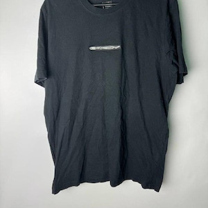May include: Black t-shirt with a small, rectangular silver and white logo on the chest. The shirt is hanging on a black hanger against a plain white background. The t-shirt is made of a soft material.