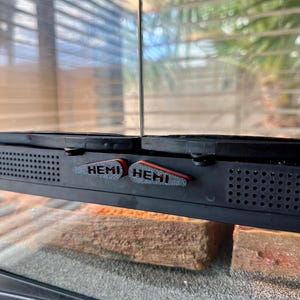 Peut inclure: Gros plan sur un terrarium noir avec deux étiquettes "HEMI" noires et rouges sur le dessus.