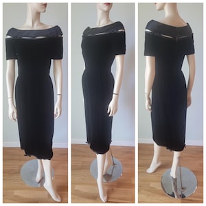 May include: A black velvet midi dress featuring an off-the-shoulder neckline with a satin collar overlay, short sleeves, and a straight skirt silhouette. The garment includes small decorative bows at the shoulders and hemline, with a back zipper.