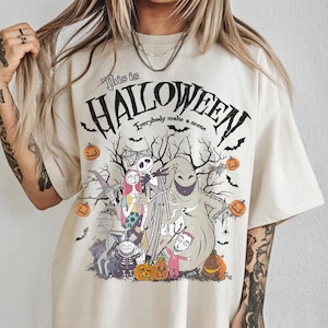 May include: Cream-colored t-shirt featuring a Halloween-themed graphic. The design includes characters, pumpkins, bats, and the text "This is Halloween, Everybody make a scene." The shirt has a relaxed fit.