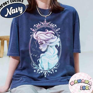 Op de afbeelding: Marineblauwe Comfort Colors T-shirt met een aquarel illustratie van een vrouw met lang, golvend haar in een ovale lijst. Het shirt heeft de tekst "Comfort Colors Navy" in een cirkelvormig ontwerp. Het shirt is van "WANANA SHOP".