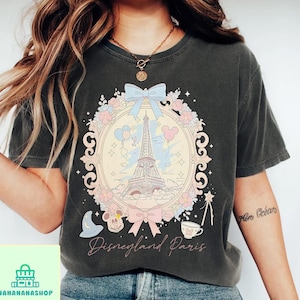 Peut inclure: T-shirt gris fonc&eacute; avec un motif Disneyland Paris. Le graphisme comprend la Tour Eiffel, Mickey Mouse et des n&oelig;uds d&eacute;coratifs. Les mots "Disneyland Paris" sont &eacute;crits en &eacute;criture cursive.