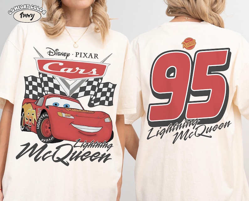 May include: Ivory-colored t-shirt featuring a graphic of Lightning McQueen from Disney Pixar's Cars. The front displays the Cars logo, a checkered flag, and the character. The back shows a large red '95' and the text 'Lightning McQueen'.