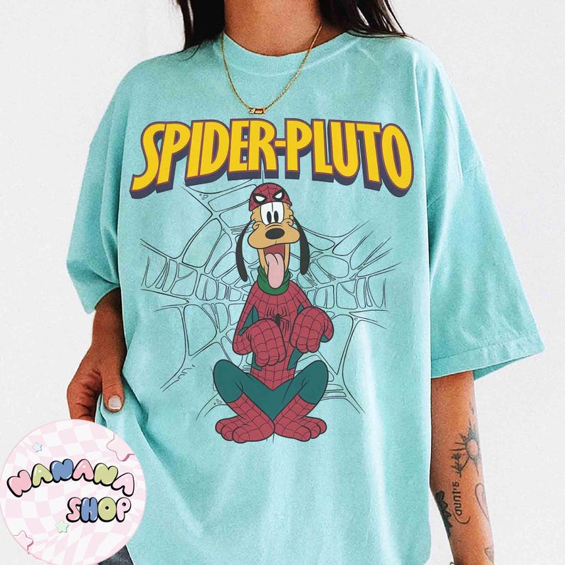 May include: A light blue t-shirt featuring a cartoon illustration of Pluto dressed as Spider-Man, with the words "SPIDER-PLUTO" in yellow block letters. The design includes a spider web background.