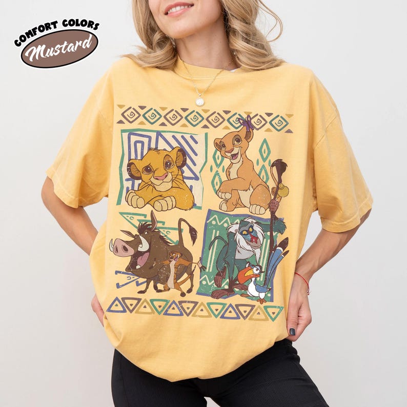 May include: Mustard-colored t-shirt featuring characters from The Lion King. The design includes Simba, Nala, Pumbaa, Timon, and Zazu, set against geometric patterns. The shirt has the words "Comfort Colors" and "Mustard" in a circular design.