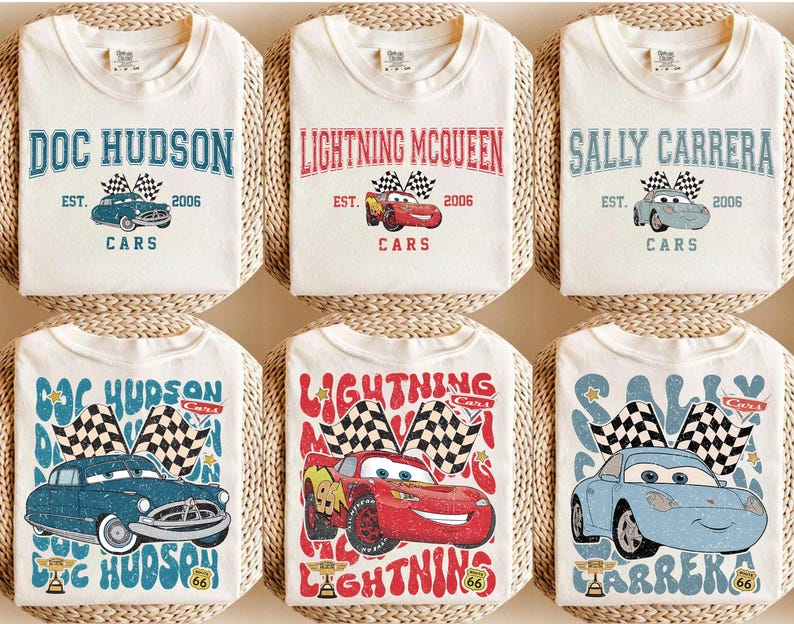 May include: White t-shirts with designs from the film "Cars." Each shirt features a character's name, a car illustration, and the year 2006. The designs include Doc Hudson, Lightning McQueen, and Sally Carrera, with checkered flags.