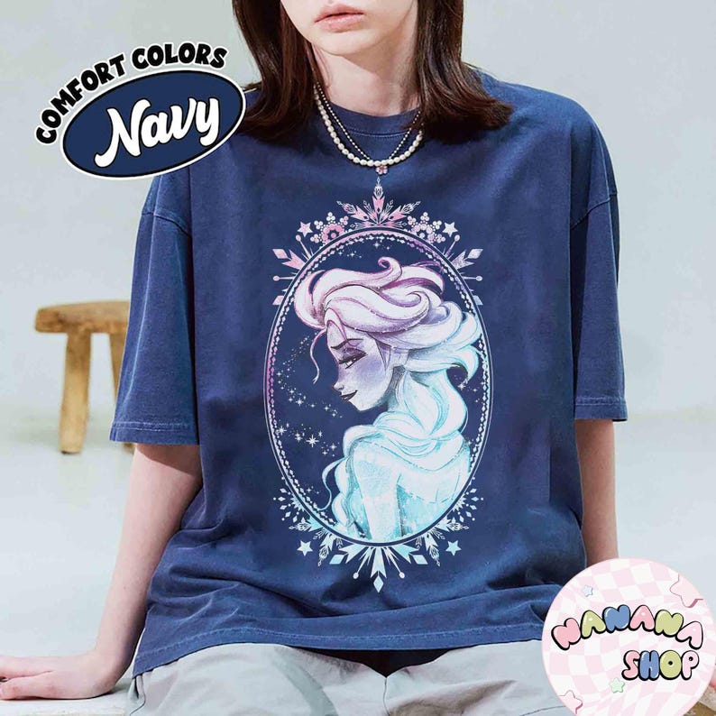 Op de afbeelding: Marineblauwe Comfort Colors T-shirt met een aquarel illustratie van een vrouw met lang, golvend haar in een ovale lijst. Het shirt heeft de tekst "Comfort Colors Navy" in een cirkelvormig ontwerp. Het shirt is van "WANANA SHOP".